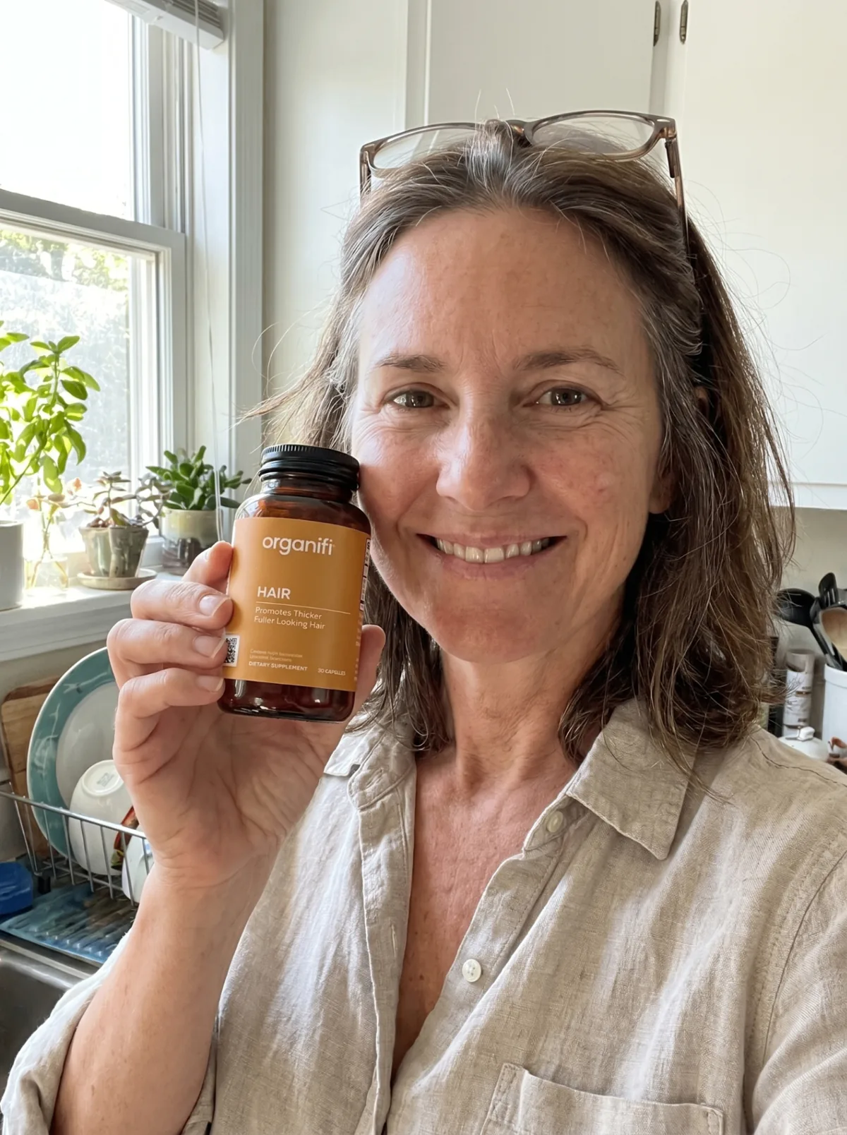 Carol holding a bottle of Organifi Hair at home
